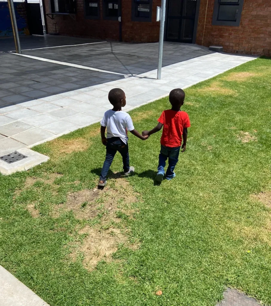Zwei kleine Kinder gehen Hand in Hand über eine Wiese im Hof des Community Center.